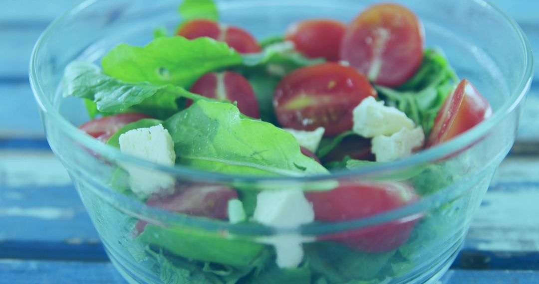 Rustic arugula salad with halved cherry tomatoes and crumbled feta in clear glass bowl