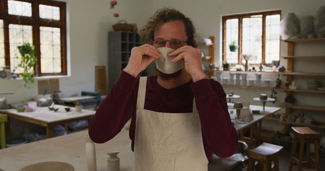 Male Potter in Home Studio Wearing Apron Adjusting Face Mask - Free Images, Stock Photos and Pictures on Pikwizard.com