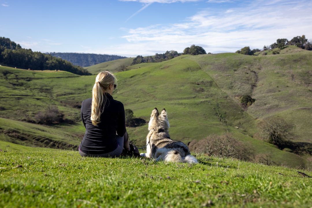 Woman Relaxing with Dog on Green Hillside