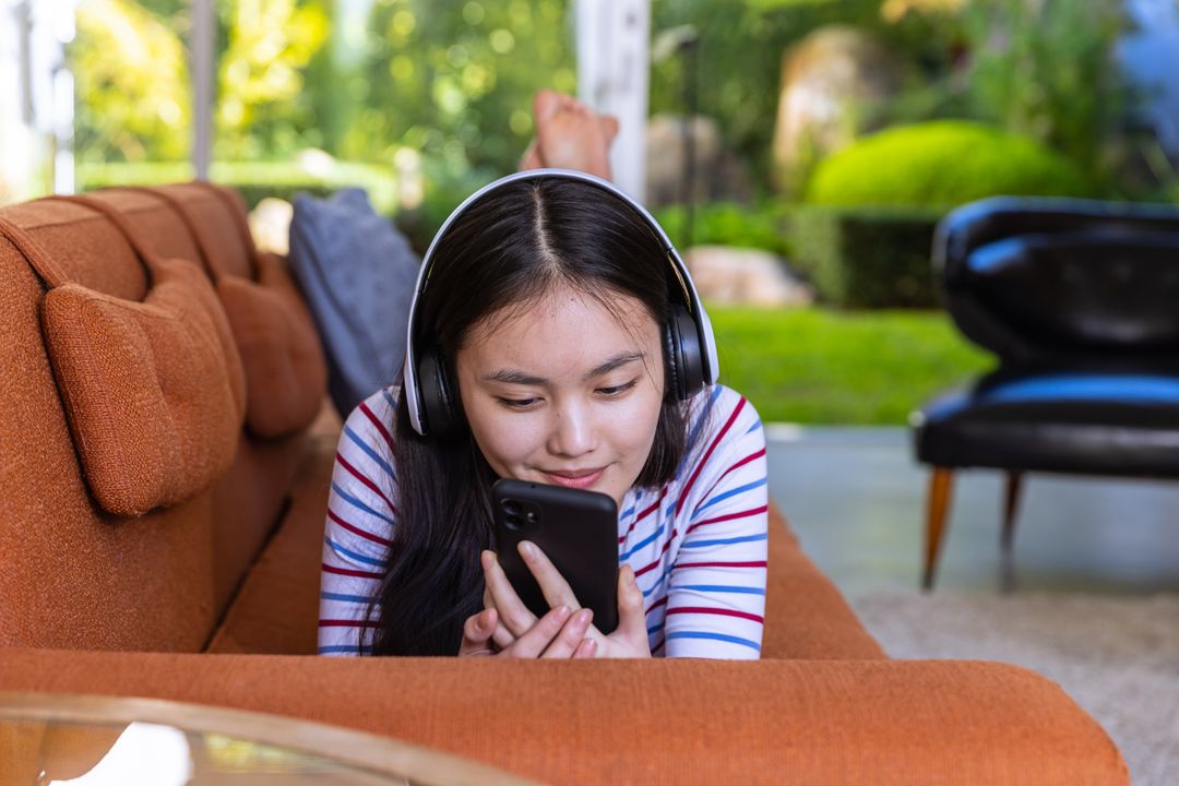 Woman Wearing Headphones Relaxing on a Sofa Using Smartphone