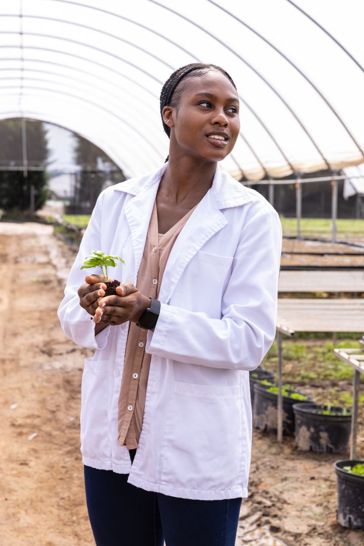 Female Botanist Analyzing Seedling in Modern Greenhouse