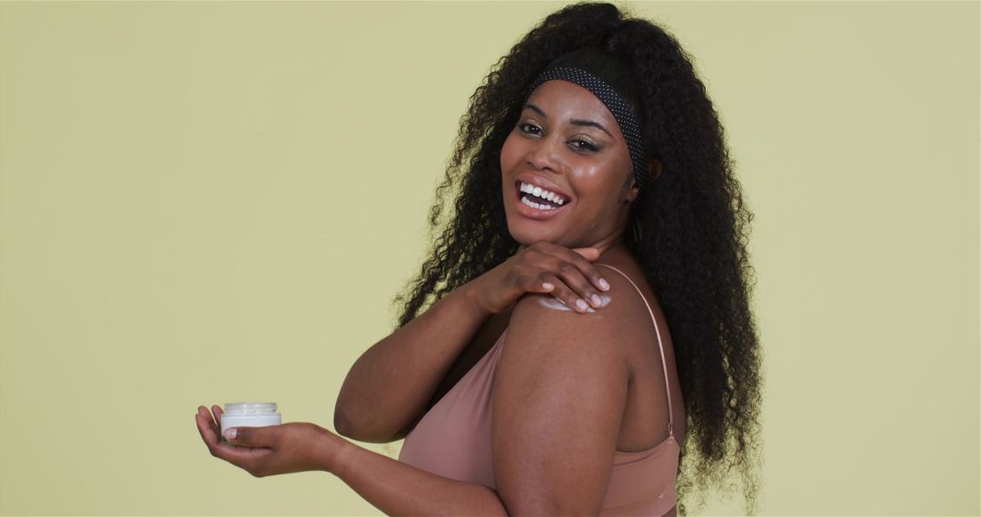 Smiling woman applying skincare cream on shoulder