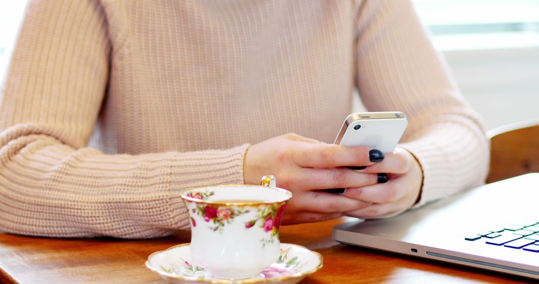 Woman Texting on Smartphone at Coffee Table with Teacup and Laptop - Free Images, Stock Photos and Pictures on Pikwizard.com