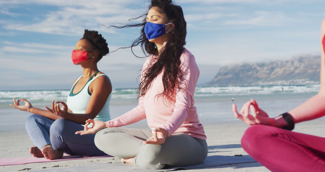 Group of diverse female friends wearing face masks meditating at the beach - Free Images, Stock Photos and Pictures on Pikwizard.com