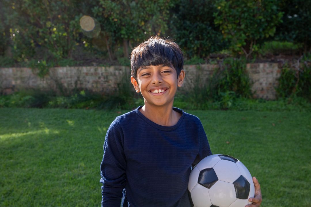 Smiling Boy Holding Soccer Ball in Lush Green Backyard