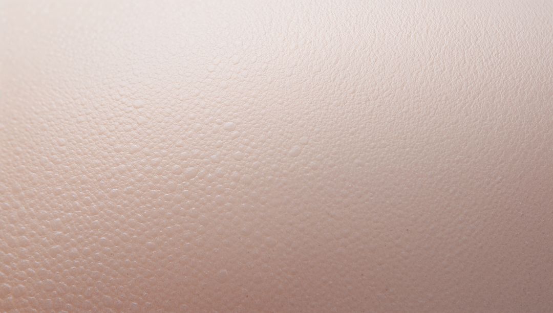 Macro closeup of pale pink pebbled skin-like texture showing fine pores and tiny droplets