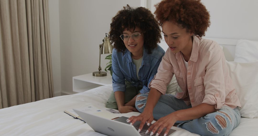 Friends collaborating on laptop while sitting on bed, planning project and studying