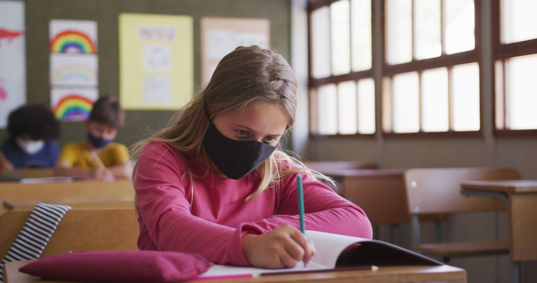 Girl in Classroom Wearing Facemask Writing in Notebook