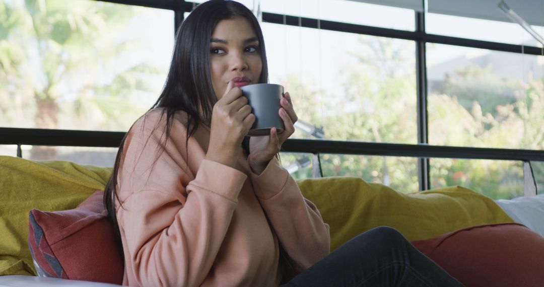 Image of happy biracial woman sitting on sofa and drinking coffee - Free Images, Stock Photos and Pictures on Pikwizard.com