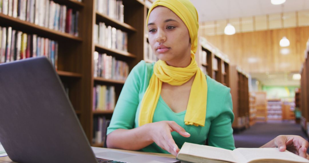 Young Woman in Hijab Studying in Library with Laptop and Book - Free Images, Stock Photos and Pictures on Pikwizard.com