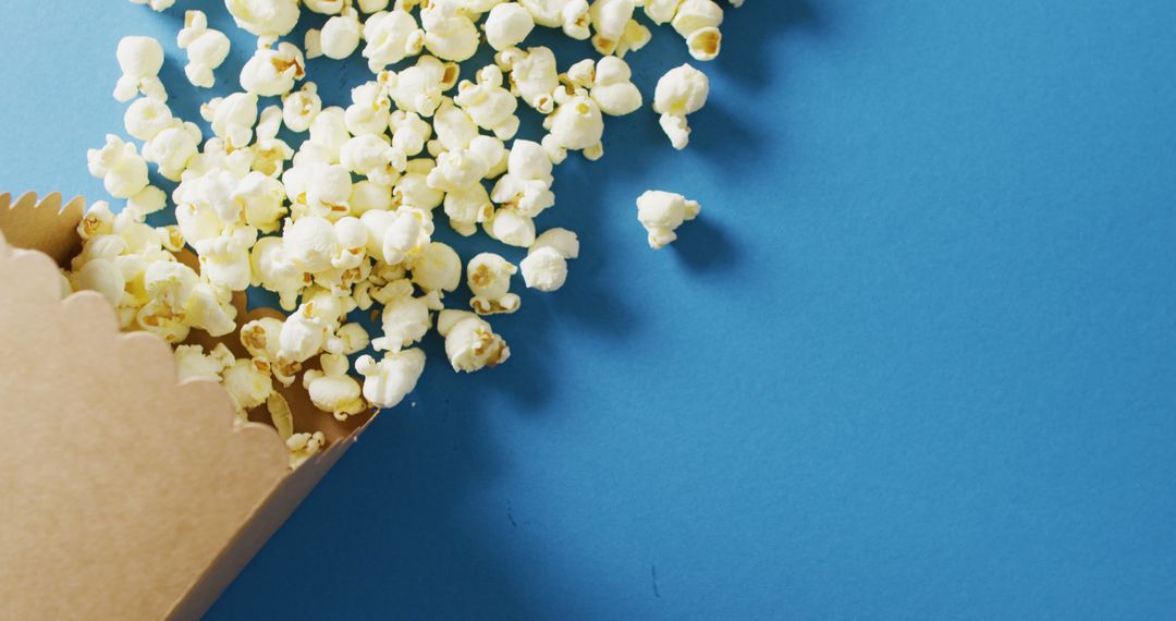 Spilled Popcorn on Blue Background for Snack Advertisements - Free Images, Stock Photos and Pictures on Pikwizard.com