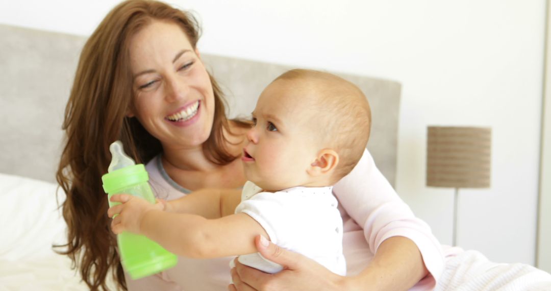 Smiling Mother Holding Baby with Bottle in Bright Room - Free Images, Stock Photos and Pictures on Pikwizard.com