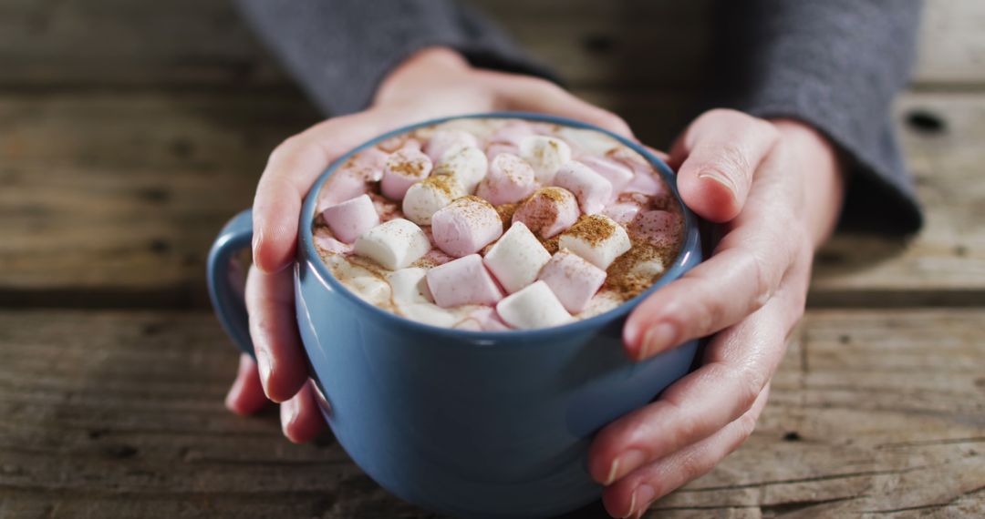 Close up view of hands holding a hot chocolate with marshmallows against wooden surface - Free Images, Stock Photos and Pictures on Pikwizard.com