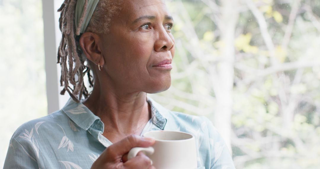 Older woman with cup of coffee looking out window thoughtfully - Free Images, Stock Photos and Pictures on Pikwizard.com