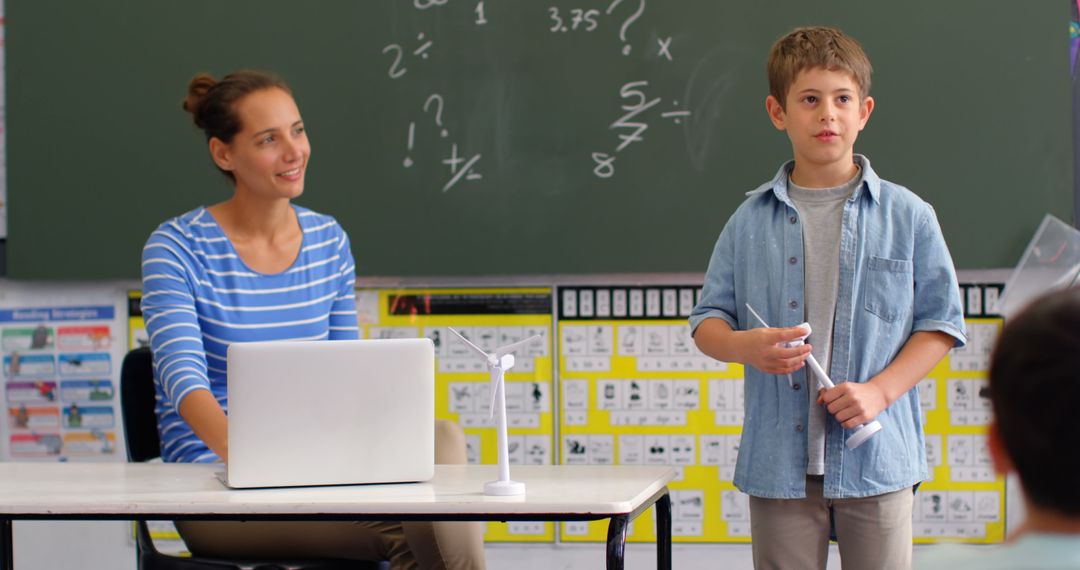 Schoolboy Presenting Windmill Model in Classroom with Teacher's Support