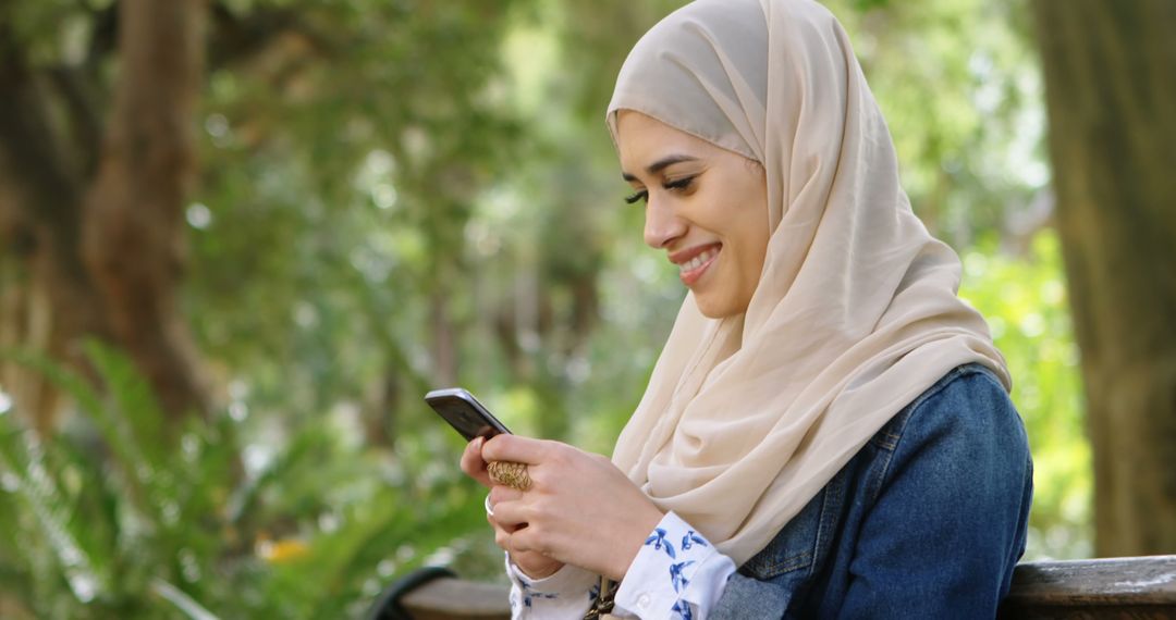 Muslim Woman Texting in Park Surrounded by Nature - Free Images, Stock Photos and Pictures on Pikwizard.com