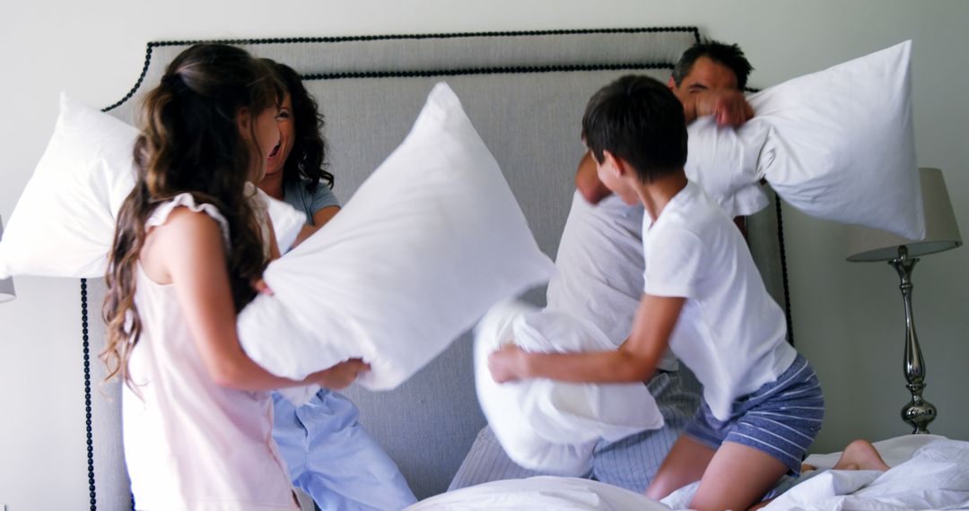 A family engages in a playful pillow fight on a bed, with copy space - Free Images, Stock Photos and Pictures on Pikwizard.com