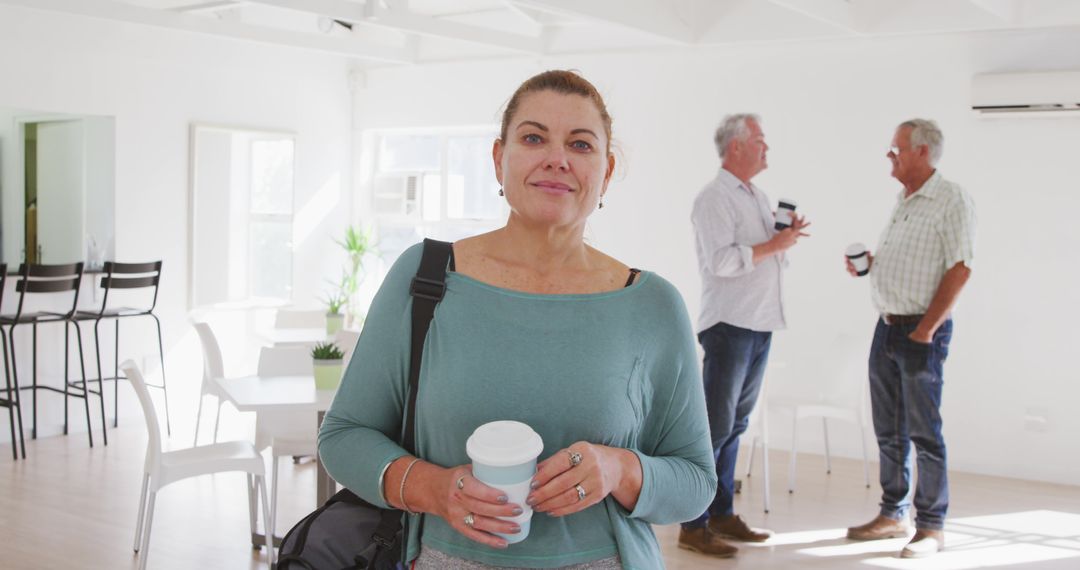 Woman holding coffee cup in bright open space with colleagues - Free Images, Stock Photos and Pictures on Pikwizard.com