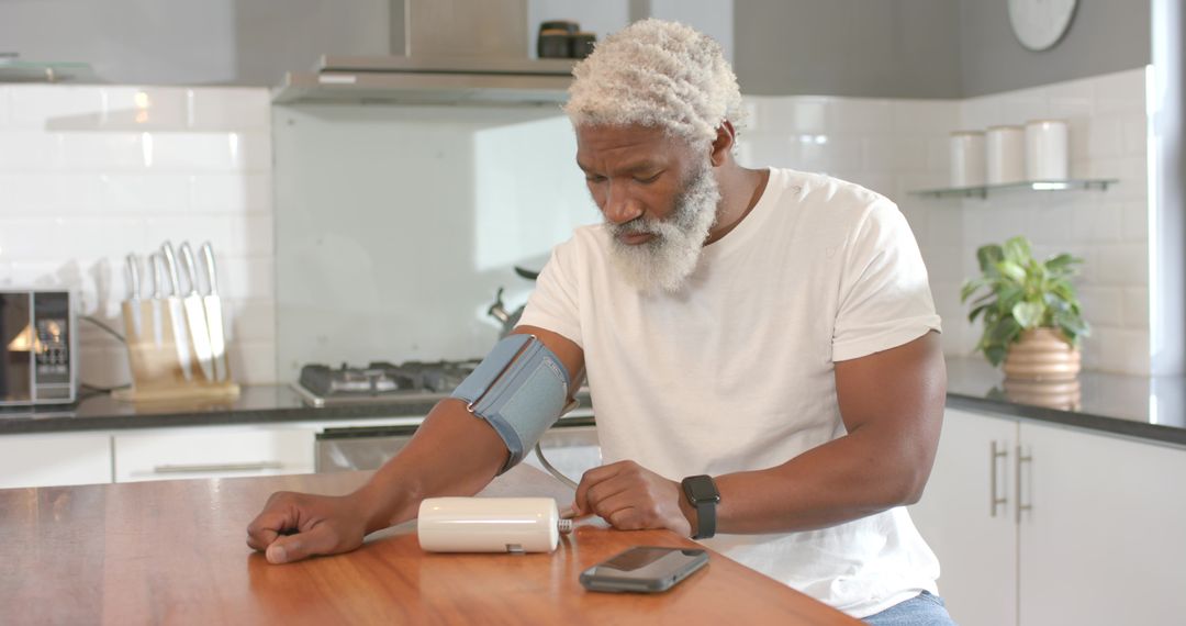Senior Man Checking Blood Pressure with Digital Cuff and Smartwatch in Kitchen