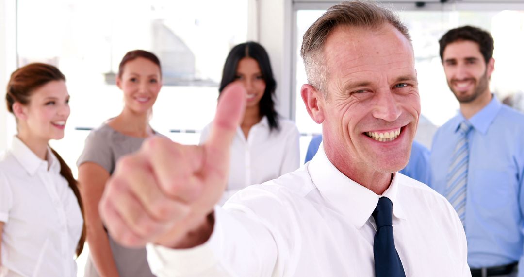 Smiling Businessman Giving Thumbs Up with Colleagues in Background - Free Images, Stock Photos and Pictures on Pikwizard.com