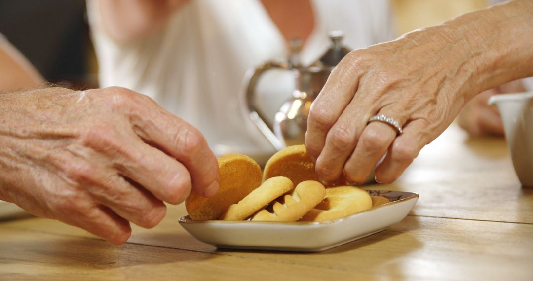 Senior Hands Reaching For Cookies on Wooden Table During Afternoon Tea - Free Images, Stock Photos and Pictures on Pikwizard.com