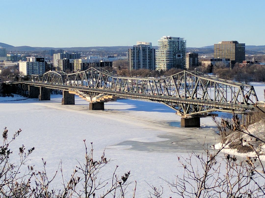 Steel bridge spanning frozen river with cityscape in background - Free Images, Stock Photos and Pictures on Pikwizard.com