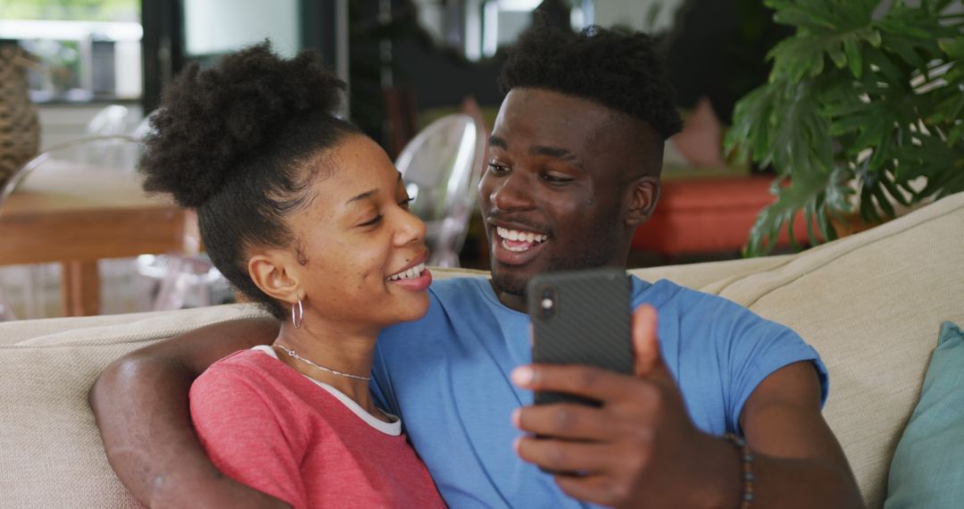 Image of happy african american couple sitting on sofa and using smartphone - Free Images, Stock Photos and Pictures on Pikwizard.com