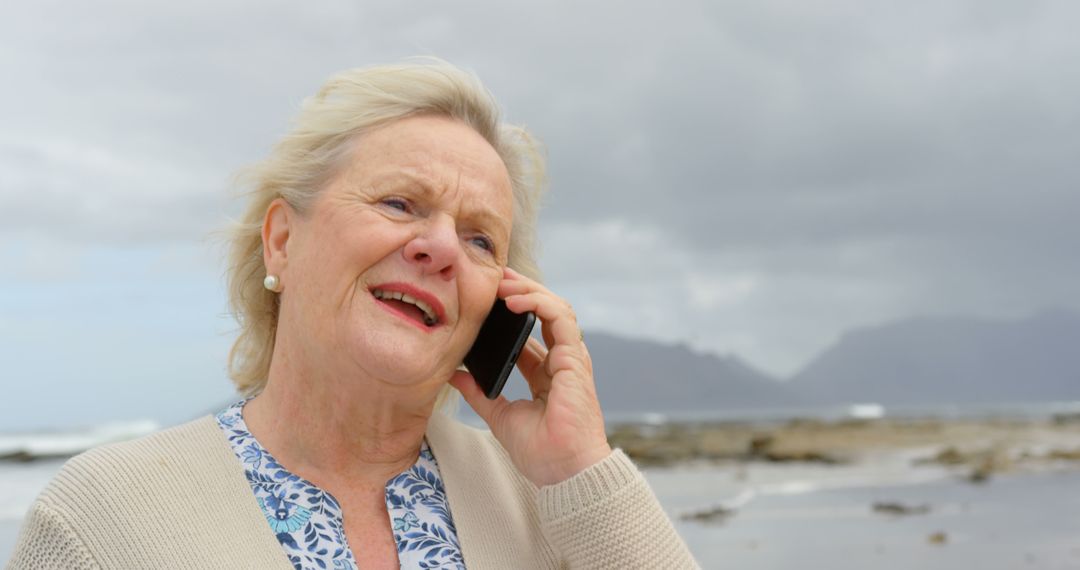 Elderly Woman Speaking on Phone at Cloudy Beach - Free Images, Stock Photos and Pictures on Pikwizard.com