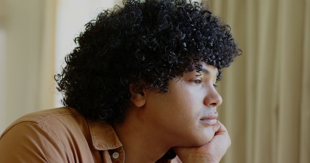 Man with Curly Hair Looking Out Window in Deep Thought