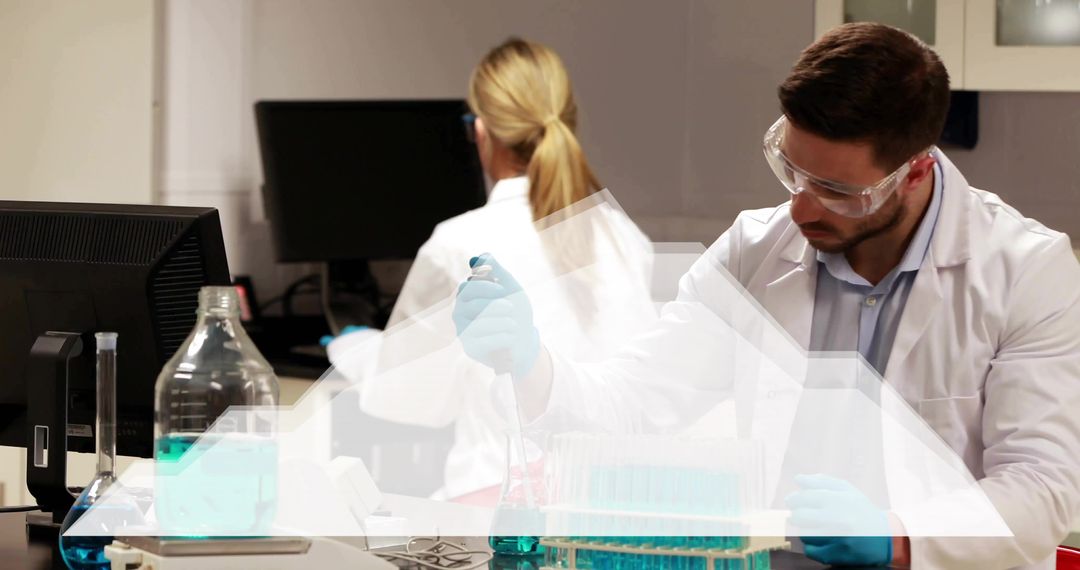 Male scientist pipetting blue reagent at lab bench while colleague working at computer