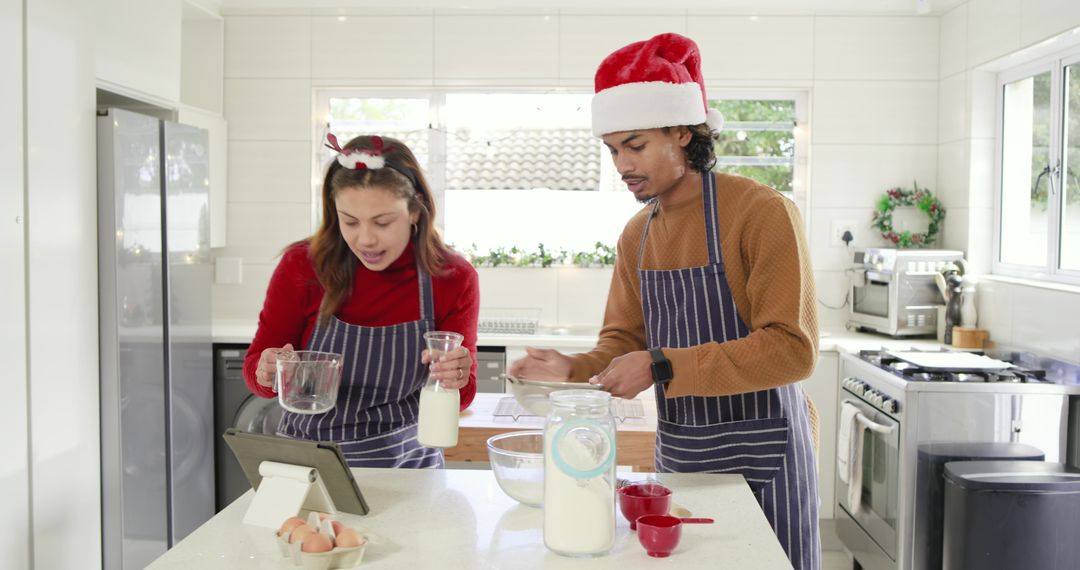 Couple preparing holiday batter in modern kitchen using tablet and striped aprons