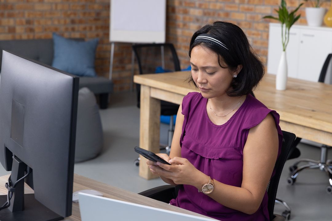 Asian Businesswoman Using Smartphone in Modern Office Workspace