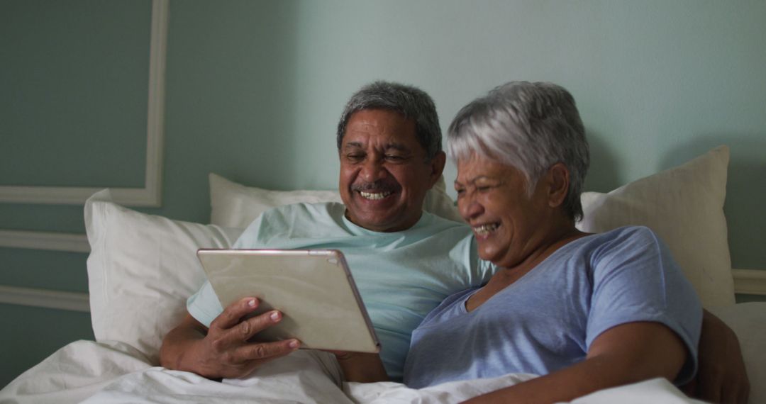 Happy Senior Couple in Bed Using Tablet for Entertainment