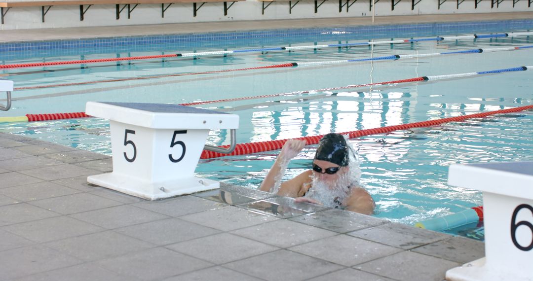 Competitive Swimmer Reaches Edge in Indoor Pool