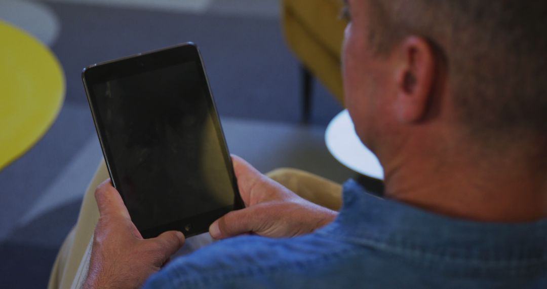 Man Using Tablet with Dark Screen in Casual Setting - Free Images, Stock Photos and Pictures on Pikwizard.com