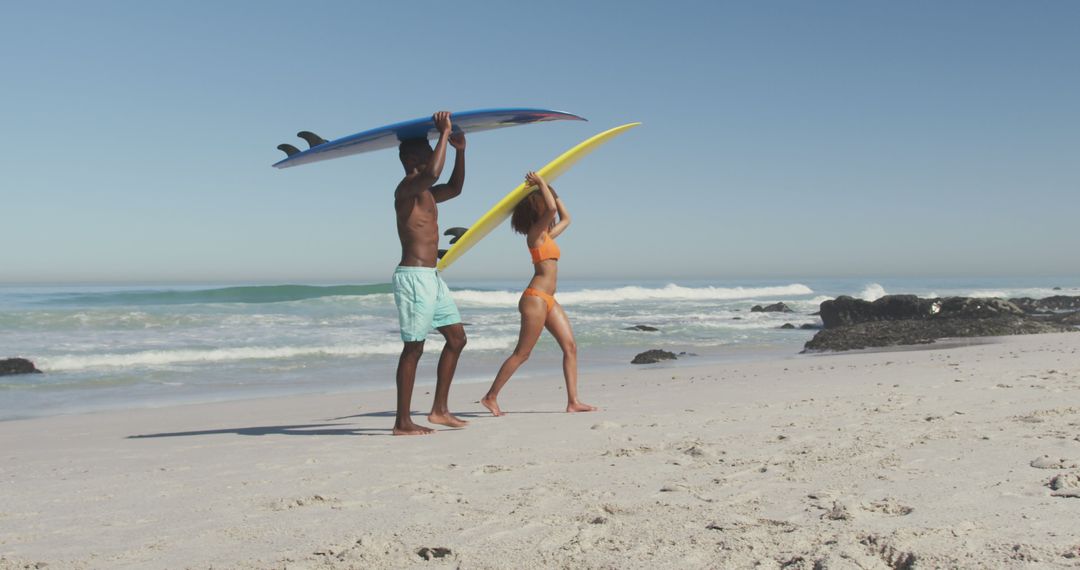 Young Man and Woman Carrying Surfboards on Sandy Beach - Free Images, Stock Photos and Pictures on Pikwizard.com