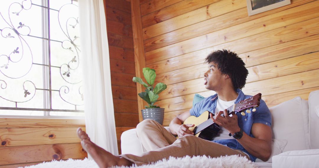 Young Man Relaxing at Home Playing Guitar by Window - Free Images, Stock Photos and Pictures on Pikwizard.com