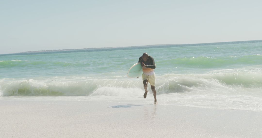 Man running along beach with surfboard on sunny day - Free Images, Stock Photos and Pictures on Pikwizard.com