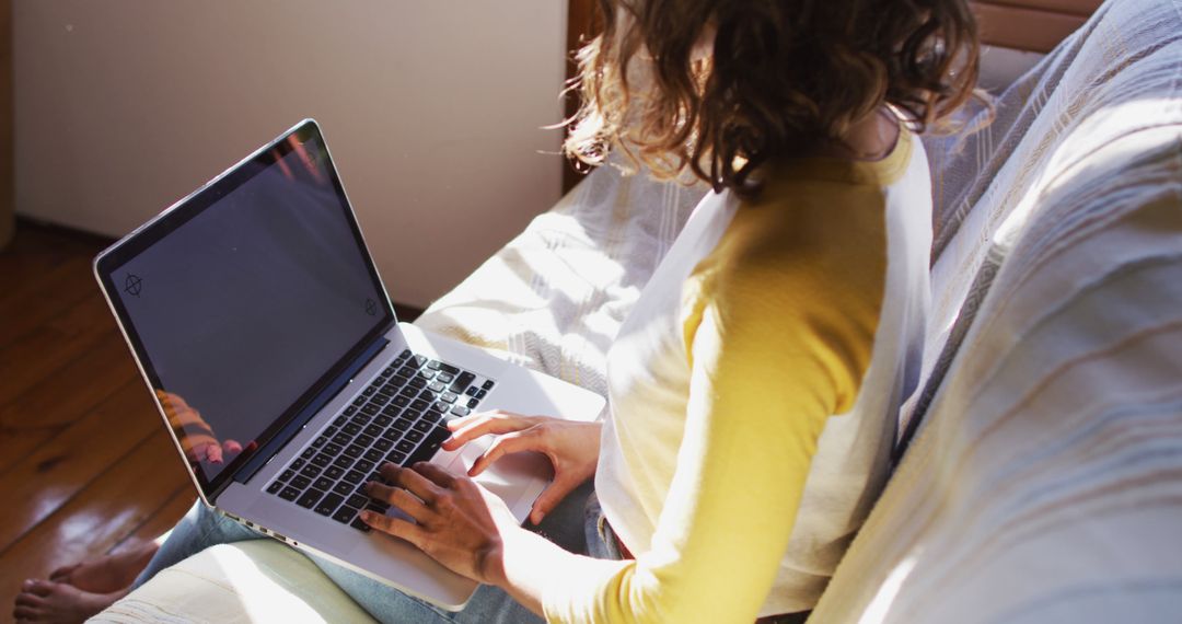 Biracial woman sitting on couch using laptop in sunny living room - Free Images, Stock Photos and Pictures on Pikwizard.com