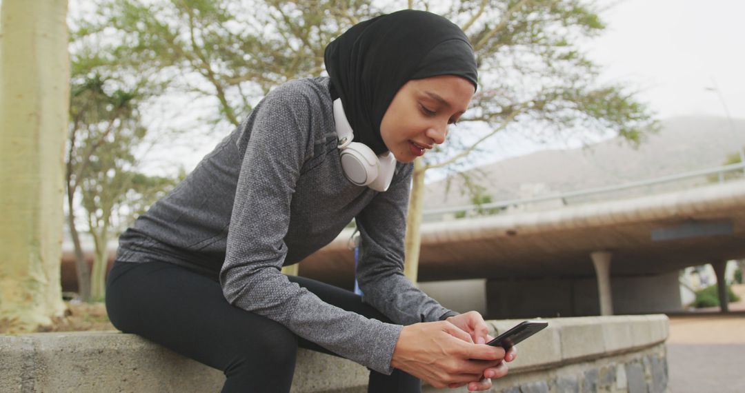 Muslim Woman Relaxing Using Smartphone with Headphones After Workout - Free Images, Stock Photos and Pictures on Pikwizard.com