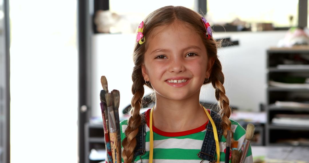 Smiling Schoolgirl Holding Paintbrushes in Art Class