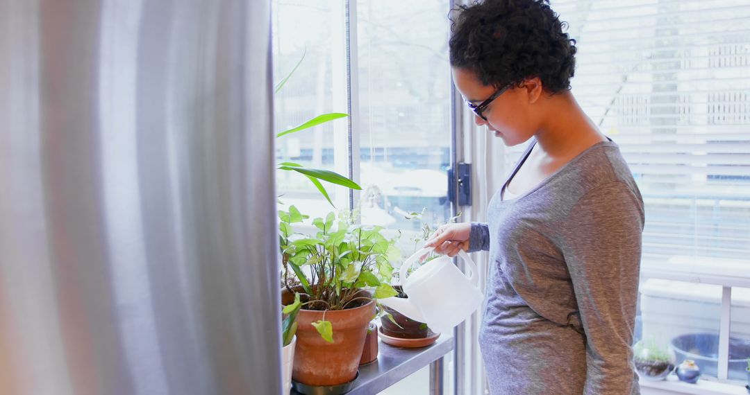 Pregnant Woman Watering Indoor Plants by Window in Natural Light - Free Images, Stock Photos and Pictures on Pikwizard.com