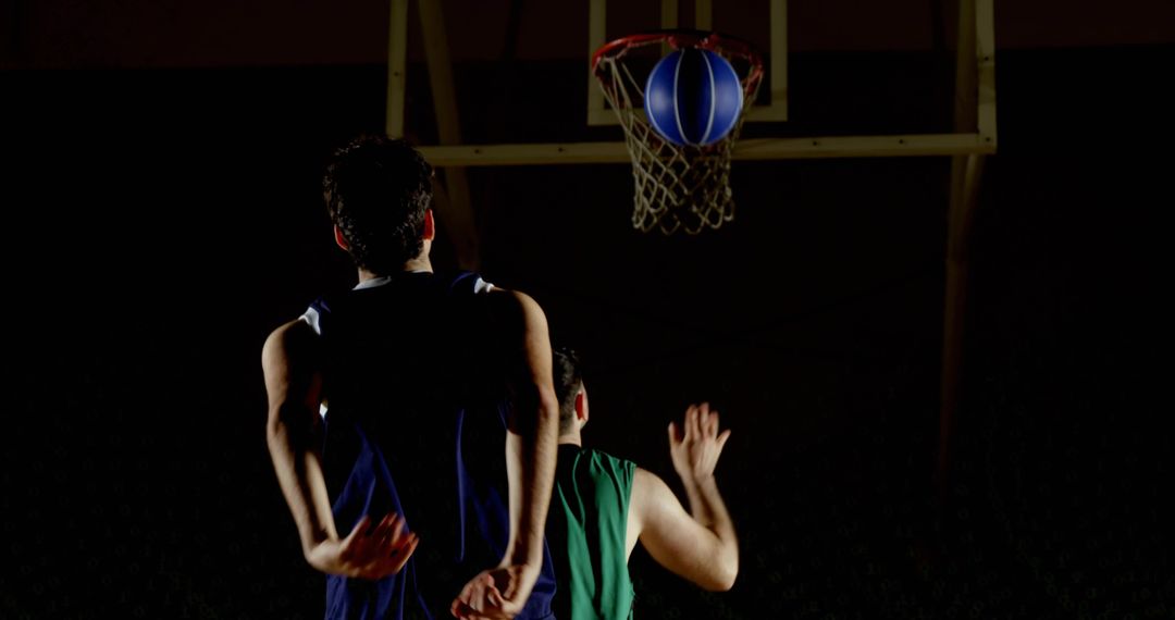 Intense Basketball Match Under Dim Gym Lighting