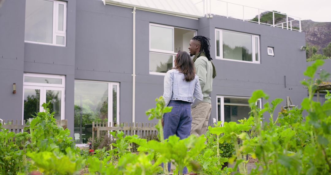 Diverse couple standing by raised garden beds in front of modern gray two-story home