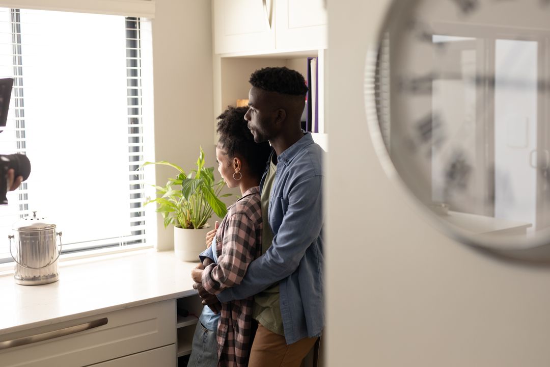 Thoughtful african american young couple looking through window while standing in kitchen at home - Free Images, Stock Photos and Pictures on Pikwizard.com