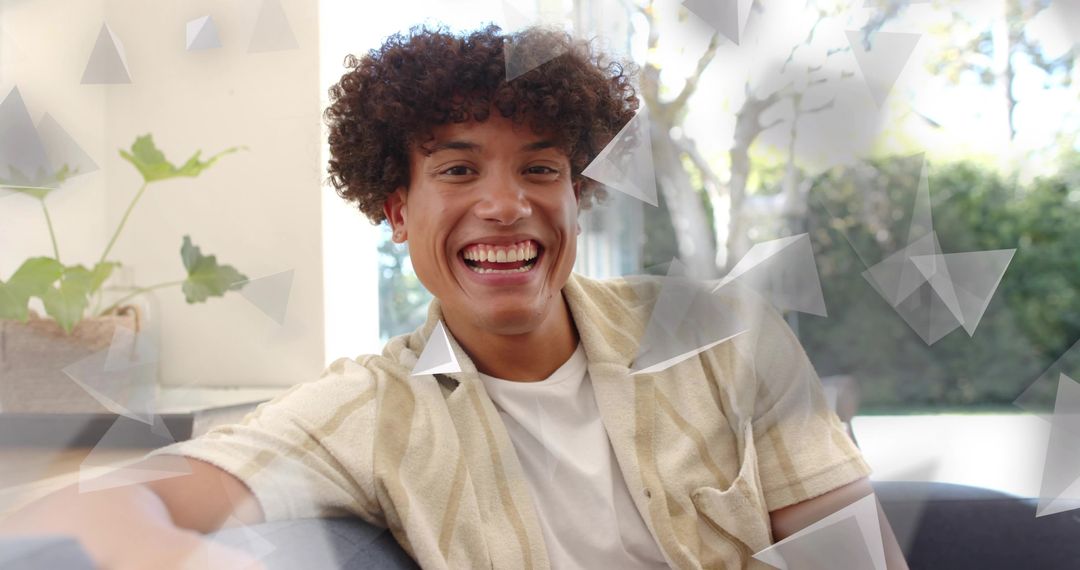 Bright smiling young man relaxing on couch with geometric overlays and indoor greenery
