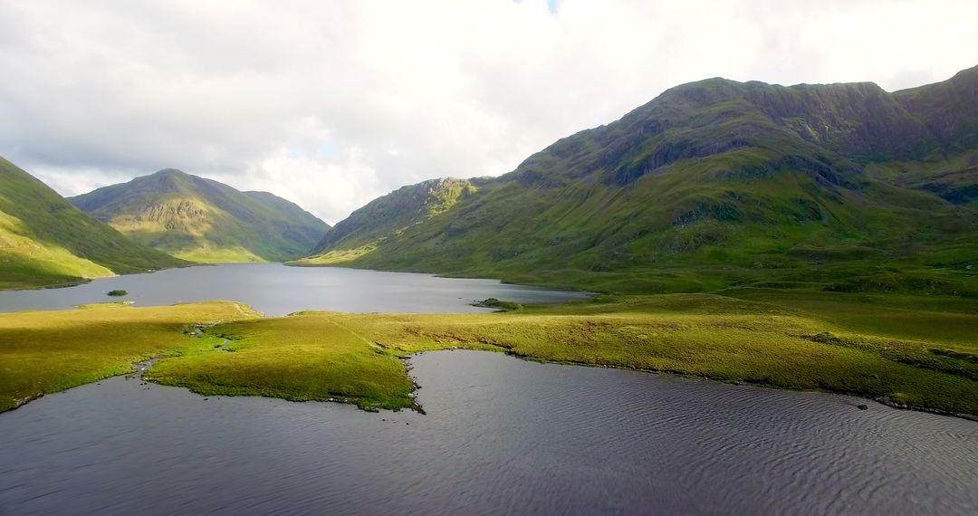 A serene landscape showcases a tranquil lake nestled among rolling green hills under a vast sky - Free Images, Stock Photos and Pictures on Pikwizard.com