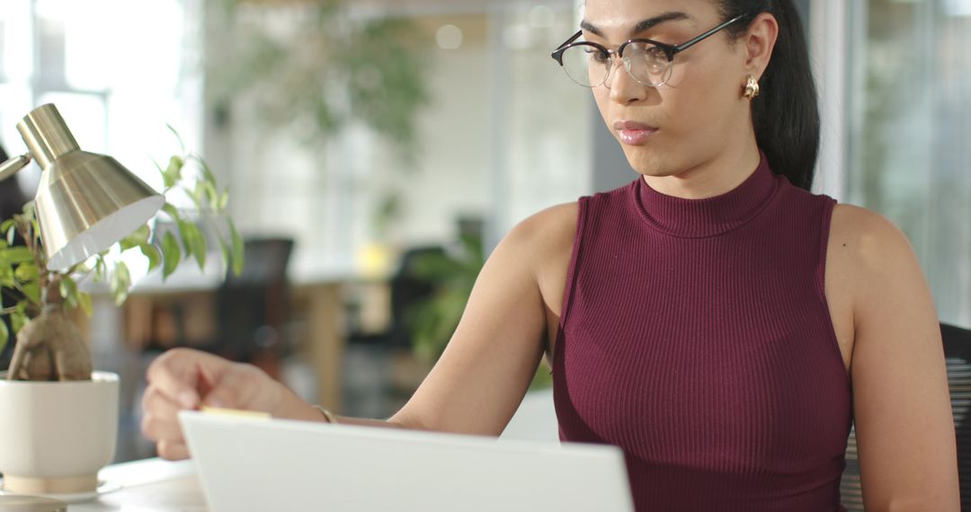 Professional woman working on laptop in modern open-plan office with natural greenery