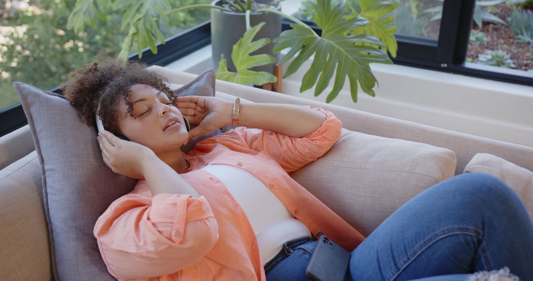 Young Woman Relaxing with Music on Cozy Couch by Window