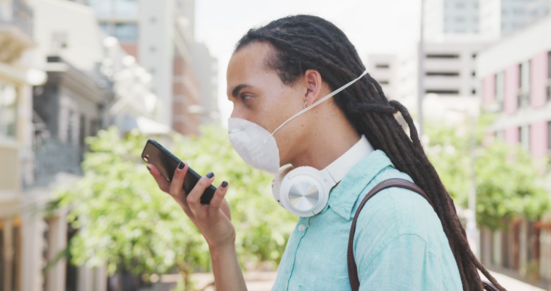 Young Man Wearing Mask and Headphones Using Smartphone Outdoors - Free Images, Stock Photos and Pictures on Pikwizard.com